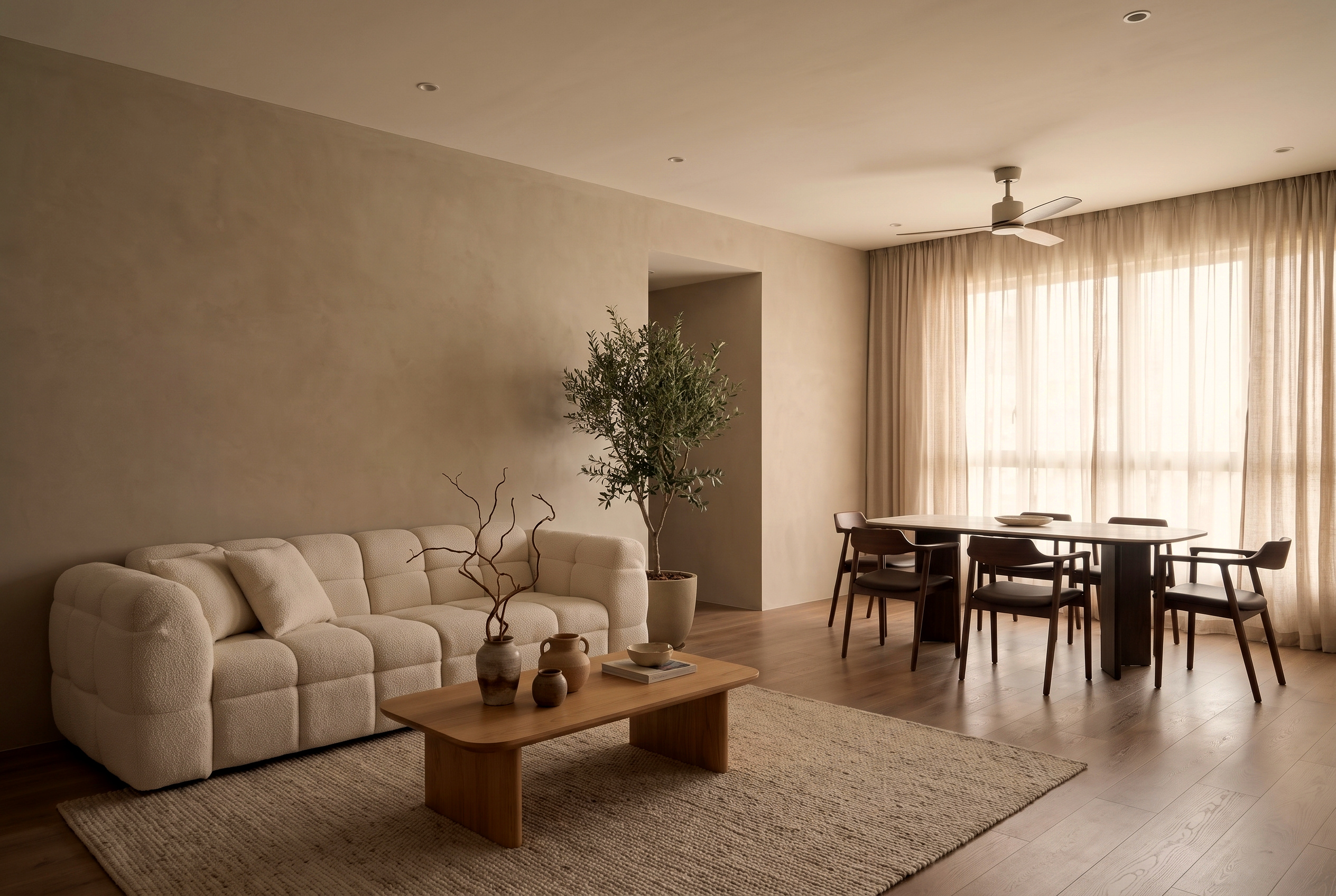 An open-plan Singapore living and dining room: a cream boucl&eacute; Son&Bear sofa and wood coffee table on a jute rug, an olive tree, and a wood dining set by sheer-curtained windows.