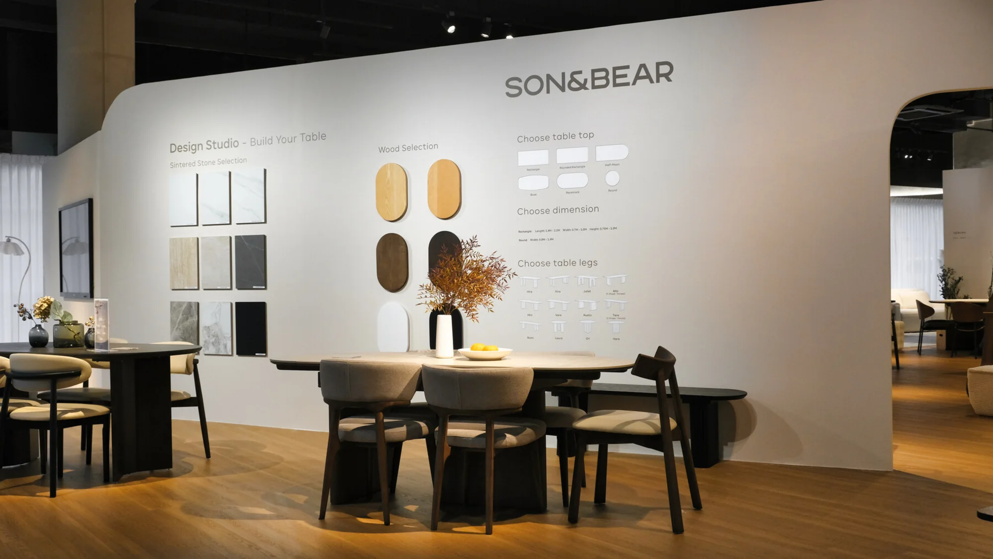 The Son&Bear showroom: the Design Studio table wall with stone and wood samples, and a dining table set beneath it.